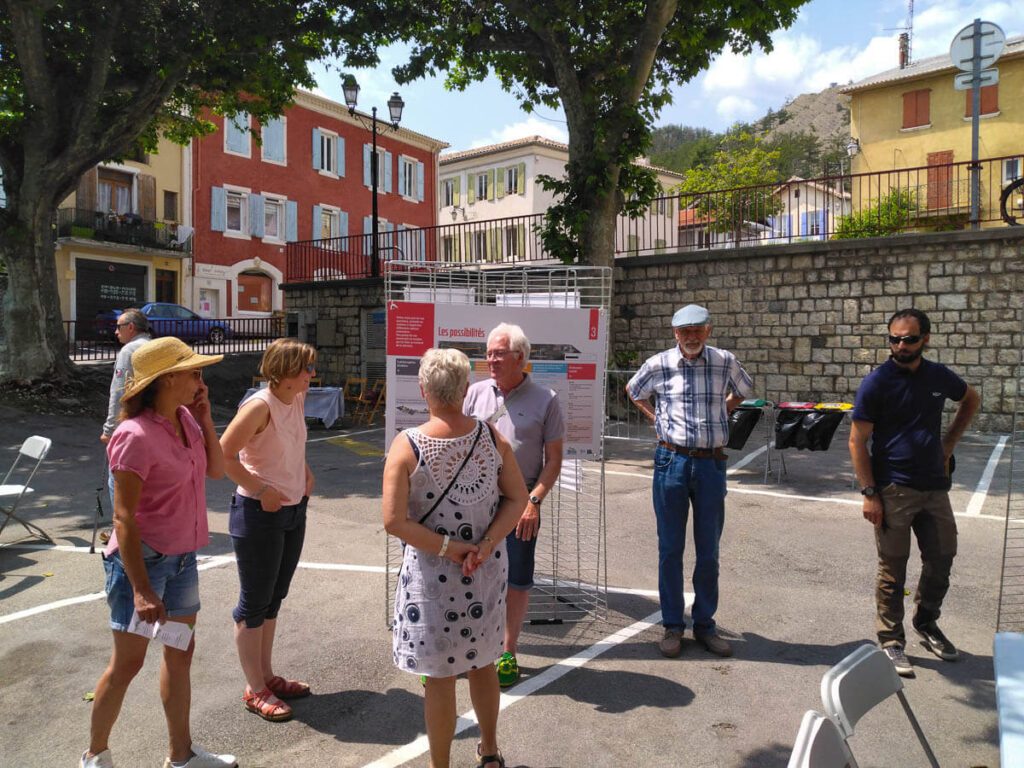 Jocelyne et Rémy sont sur la place de la mairie et discutent avec des citoyens devant les panneaux décrivant les projets d'aménagement des digues de Veynes