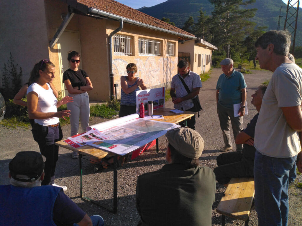 Jocelyne et Carolyne expliquent les projets d'aménagement des digues de la Roche des Arnauds aux citoyens présents autour de la table de travail aux abords du stade.